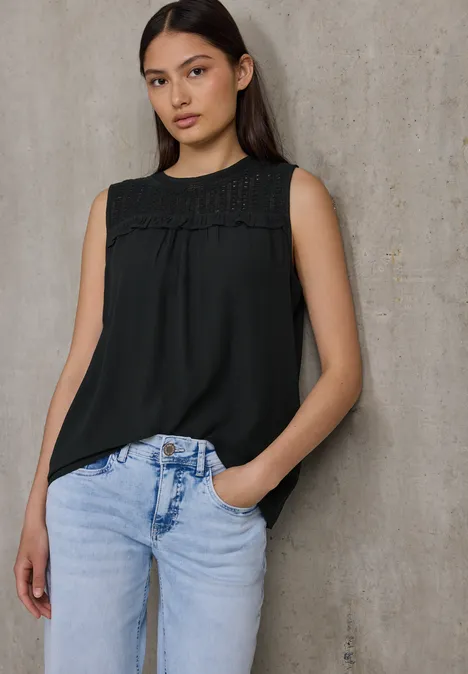 Frau mit dunkler Bluse und Jeans steht vor Betonwand.